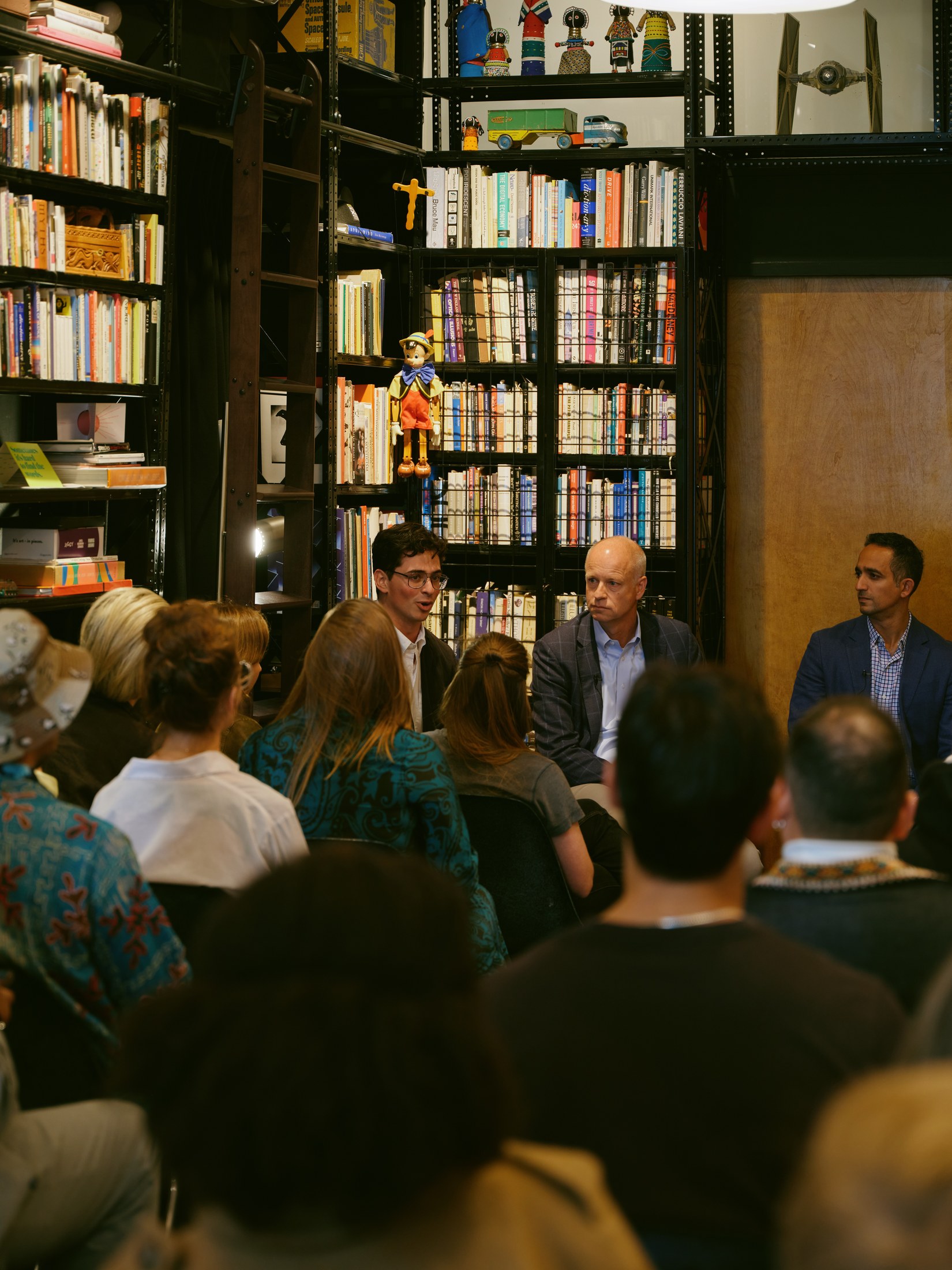 The moderator speaking with panelists among the bookshelves