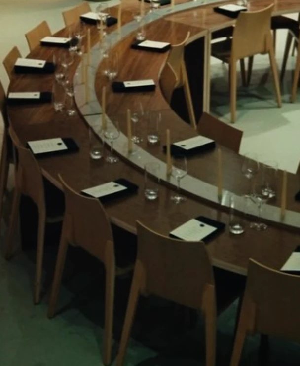 A curved wooden table set for dinner, with menus at every seat